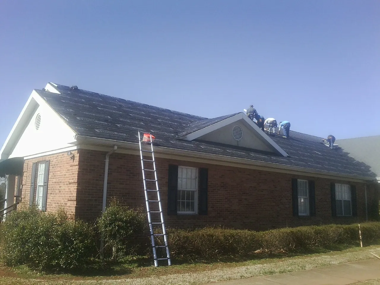 Crew tearing shingles off a brick ranch roof with a ladder set — Metal Roof Repair work by our crew in New Stuyahok