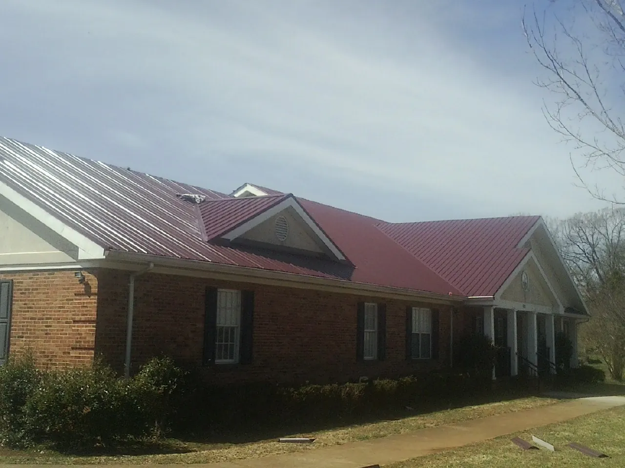 Red metal roof with gabled entries on a long brick building, from a Hail Damage Roof Repair job in New Stuyahok