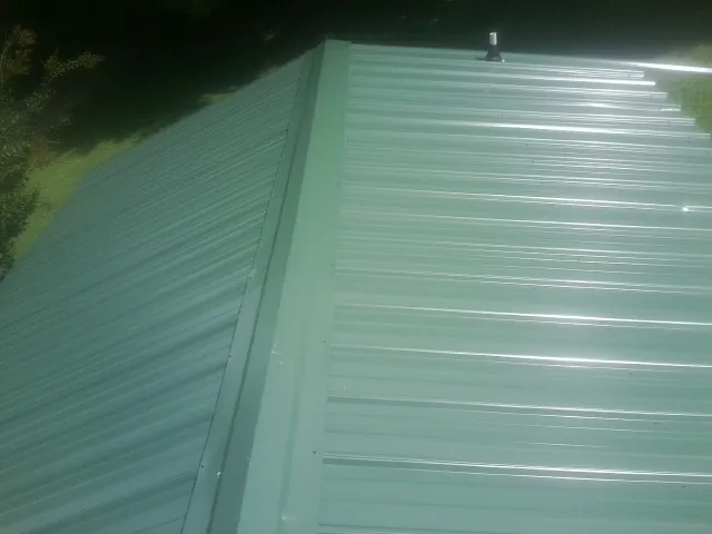 New green metal panels meeting at the ridge of a roof — Flat Roof Repair work by our crew in New Stuyahok