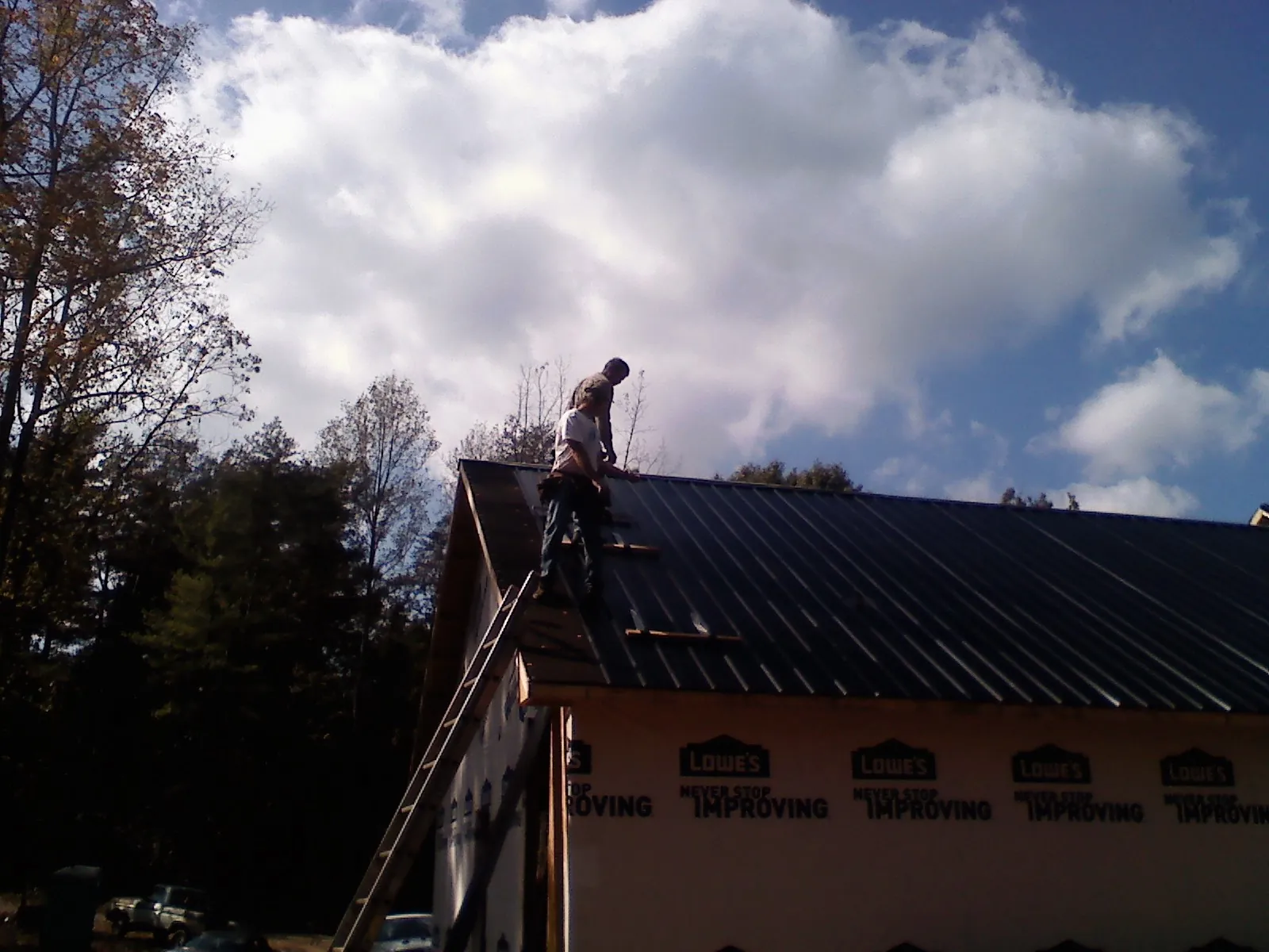 Roofer fastening dark metal panels high against a cloudy sky, from a Roof Inspection job in New Stuyahok