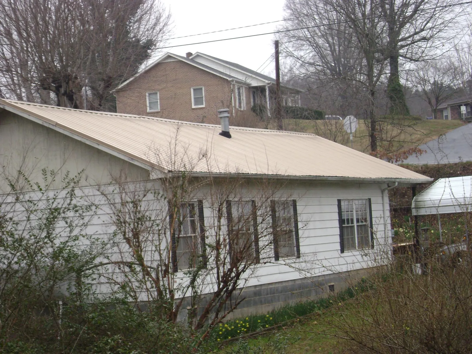 Tan metal roof on a white sided house set into a hillside — Commercial Roofing by Roofing Brothers in New Stuyahok