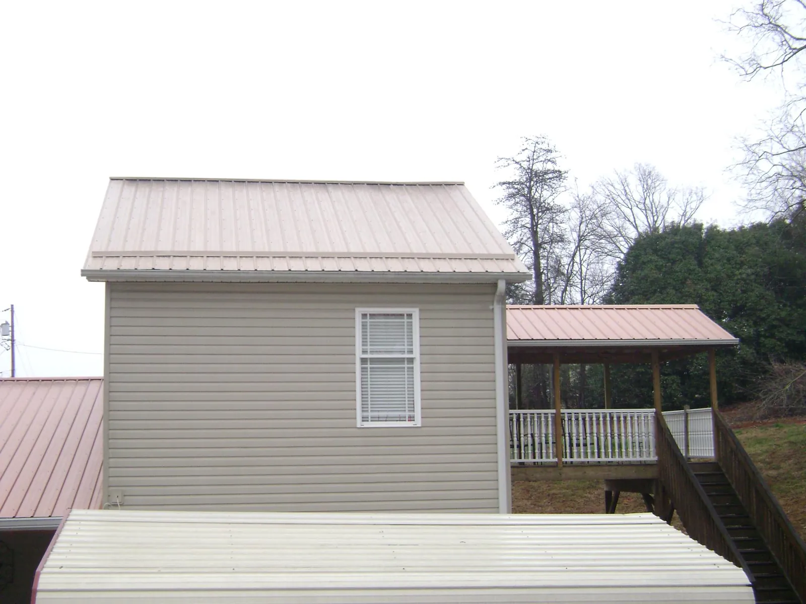 Tan metal roofs on a two story addition and attached porch, from a Roof Replacement job in New Stuyahok